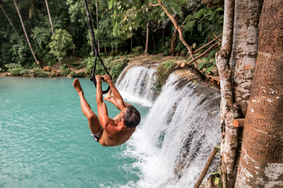 A young caucasian man plays with a rope swing over the Cambugahay Falls in Siquijor Island, Philippines